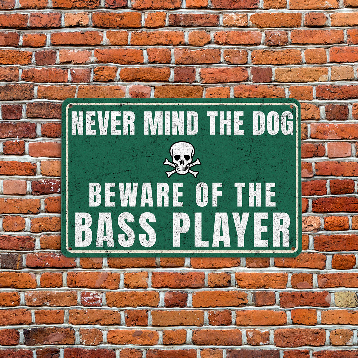 A vintage-style green metal sign with a skull and crossbones icon that reads 'Never mind the dog, beware of the bass player' mounted on a rustic wooden fence.