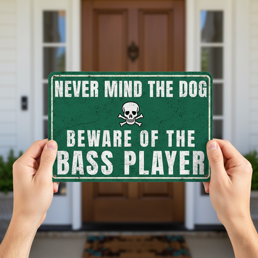 A vintage-style green metal sign with a skull and crossbones icon that reads 'Never mind the dog, beware of the bass player' mounted on a rustic wooden fence.